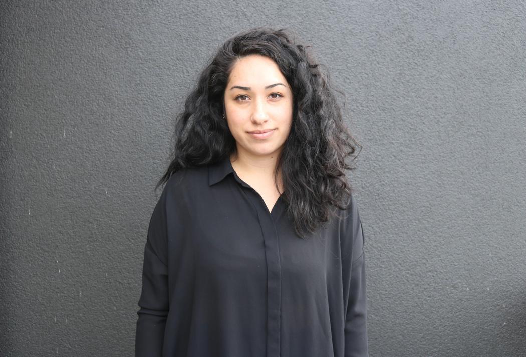 A woman looking at the camera wearing a black shirt, and a black wall behind